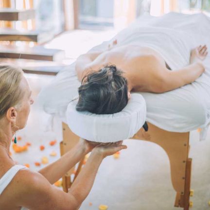 Masseuse giving a private service to a woman on a white bed surrounded by orange petals