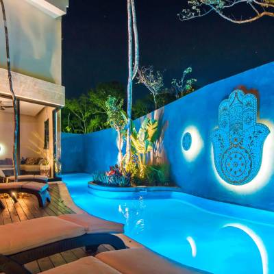 Image of the outside pool at night, hamsa hand decoration on the wall