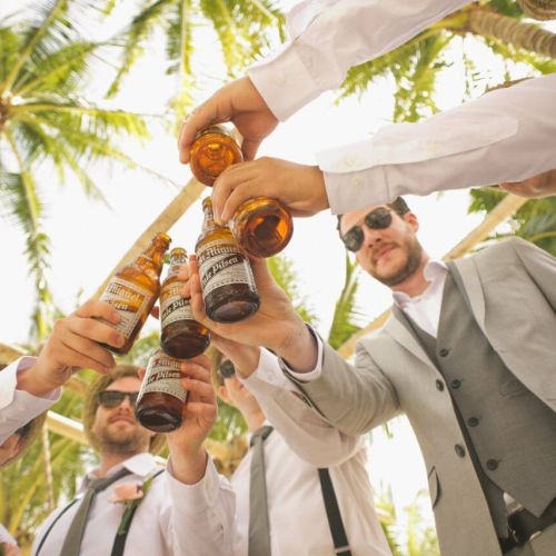 A group of men wearing suits clinking their beers on the beach