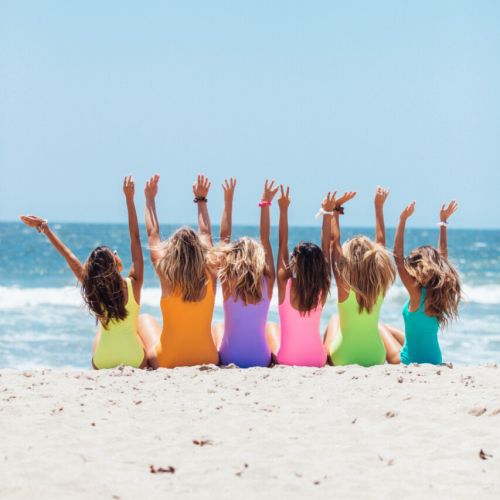 Girls sitting together at the beach wearing coordinated colorful bathing suits